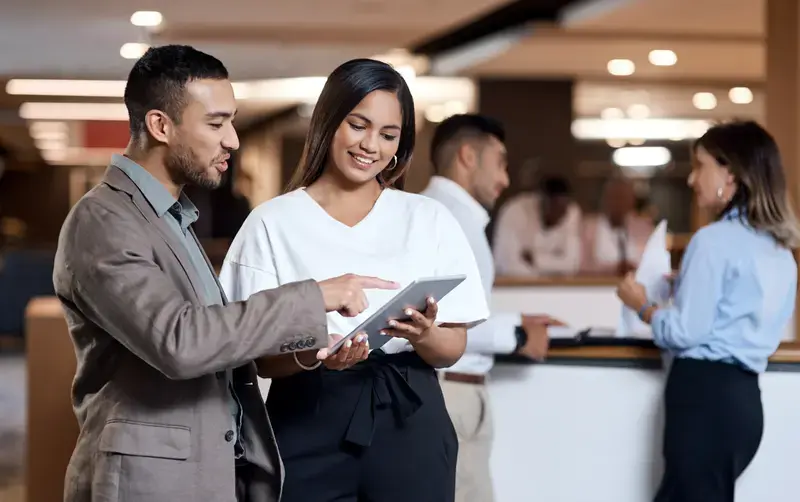 Stock - A man and a women looking on a tablet at a business event